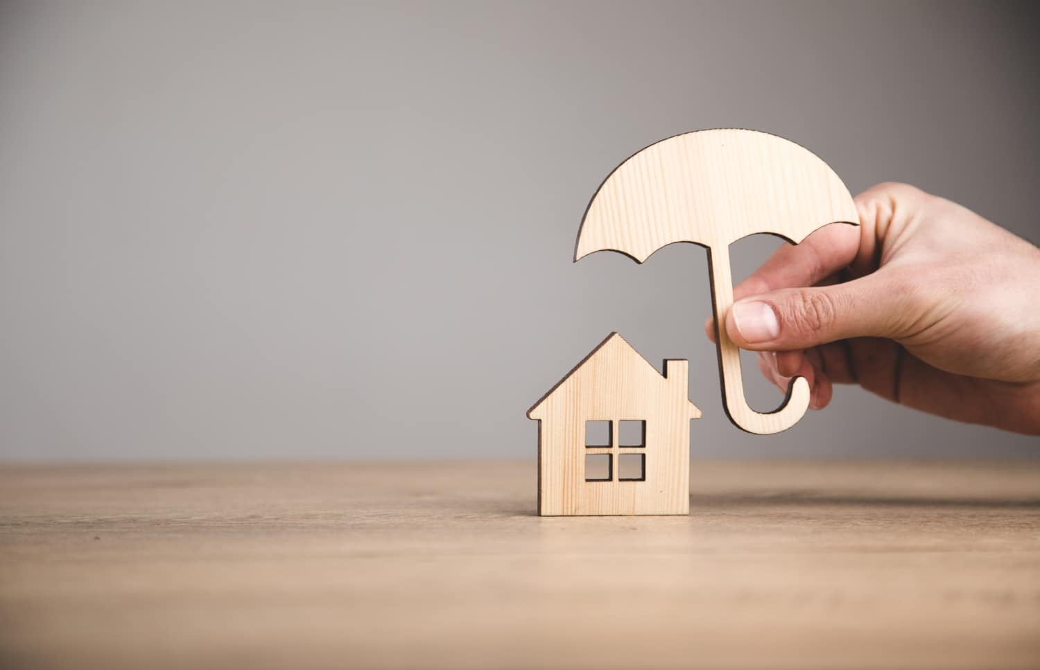 un homme tient un parapluie en bois au dessus d'une maison en bois illustrant l'assurance habitation